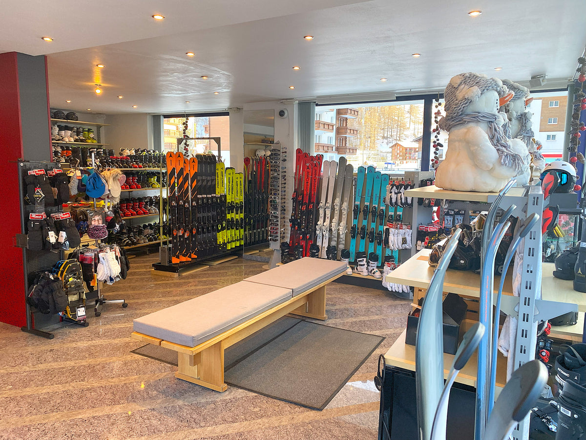 Ladeninneres mit Ski, Helmen und Sitzbank zur Skischuh-Anprobe bei Burgener SKI Sport Saas-Grund